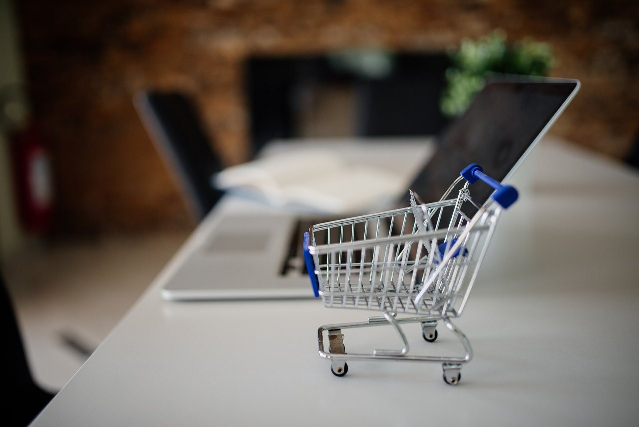 Mini shopping cart placed on a table next to a laptop in a modern office setting