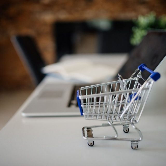 Mini shopping cart placed on a table next to a laptop in a modern office setting