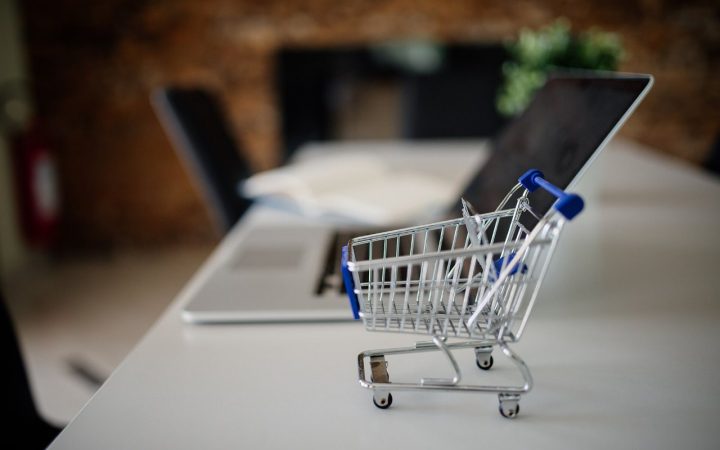 Mini shopping cart placed on a table next to a laptop in a modern office setting